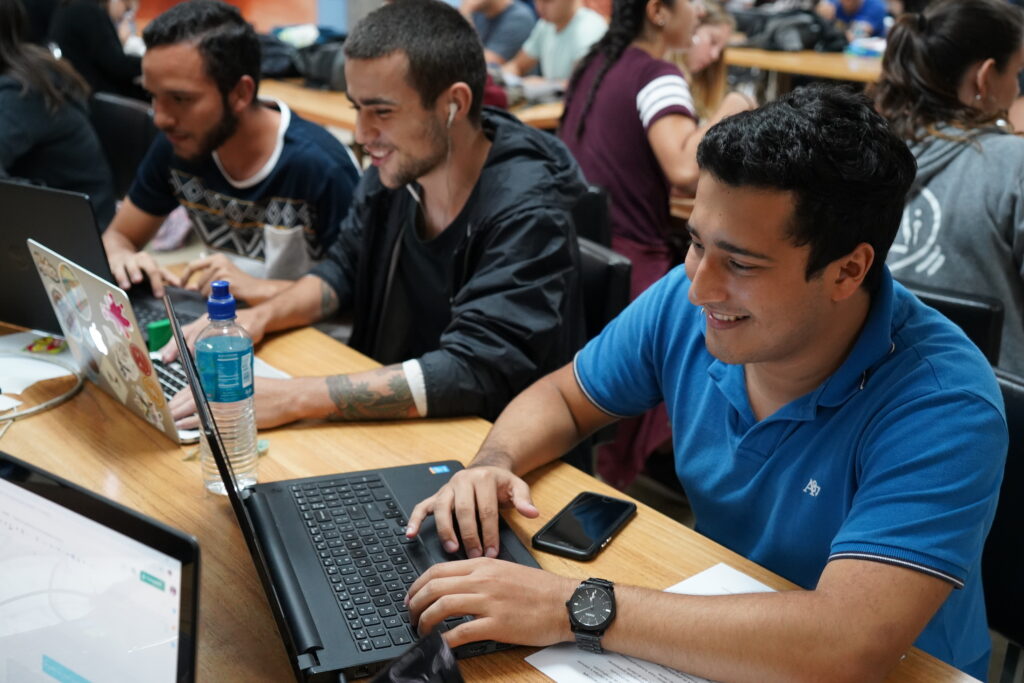 Fotografía que muestra a varios estudiantes en un ambiente de trabajo colaborativo, enfocados en sus computadoras portátiles.